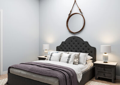 Room with upholstered grey bed, side tables, and lamps on each side.