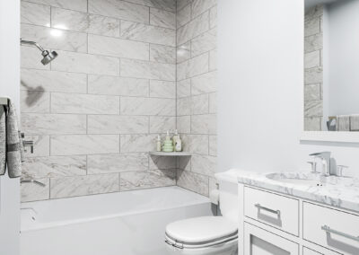 Spacious bathroom with white marble countertop and shower tiles. Grey tile flooring.