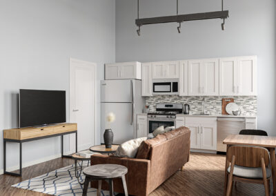 Living area next to kitchen with hardwood flooring and brown couch facing tv center.