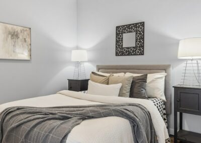 Angled view of queen bed in grey room with wire lamps on each side and decorative mirror above bed.