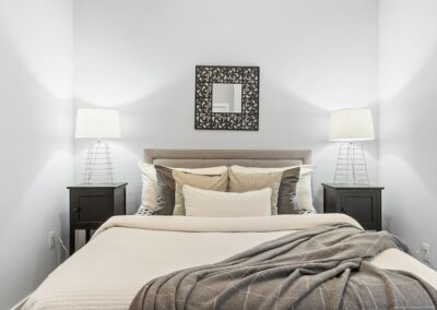 Queen bed in light grey room with wire lamps on each side and decorative mirror above bed.