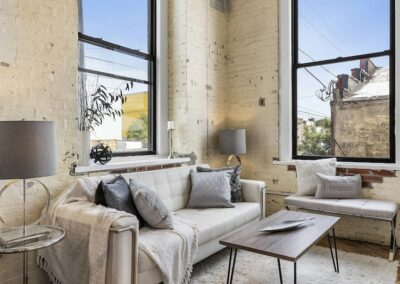 Living room with large windows, tan couch and small bench.