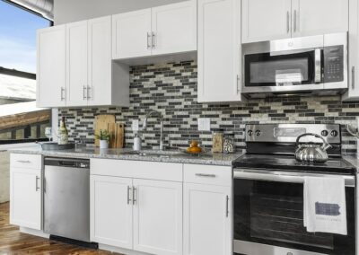 Kitchen with mosaic backsplash, granite countertop, stainless steel appliances, and white cabinets.
