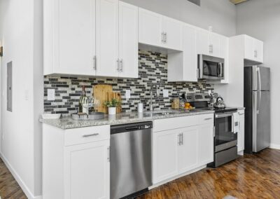 Kitchen with mosaic backsplash, granite countertops, and stainless steel appliances on wood floors.