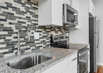 Kitchen with mosaic grey and black backsplash, granite countertops, and stainless steel appliances.