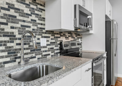 Granite countertops in kitchen with mosaic grey backsplash and stainless steel appliances.