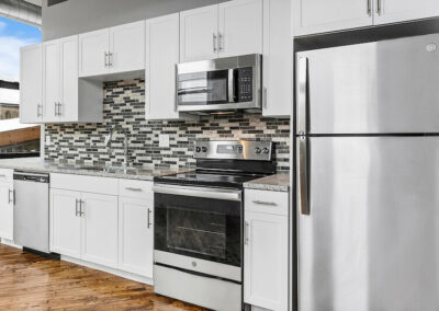 Kitchen with white cabinets, grey counters, mosaic backsplash, and stainless steel appliances.
