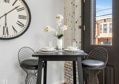 Close up of kitchen seating area with black high table, large clock, and view of street.